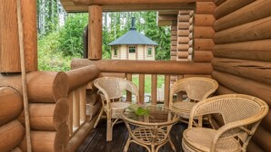 Eine Blockhütte mit einem Balkon, ausgestattet mit Korbstühlen und einem Glastisch.