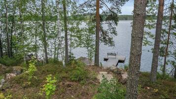 A lakeside deck with a wooden bench and a small table, surrounded by trees and a rocky shoreline.
