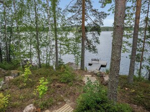 A lakeside deck with a wooden bench and a small table, surrounded by trees and a rocky shoreline. - Neitlinna by Interhome (Mikkeli)
