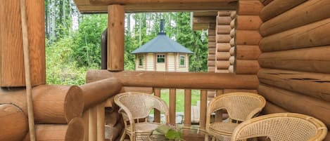 A wooden log cabin with a balcony featuring wicker chairs and a glass table.