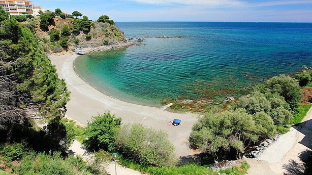 A coastal view with a clear beach, a small boat, and a building in the background. - Puerto De La Selva by Interhome (Llançà)