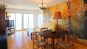 A dining area with a table and chairs, a television, and a large painting on the wall. - Puerto De La Selva by Interhome (Llançà)