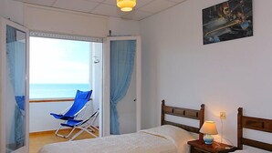A hotel room with two beds, a balcony with a view of the sea, a painting on the wall, and a lamp on the nightstand. - Puerto De La Selva by Interhome (Llançà)