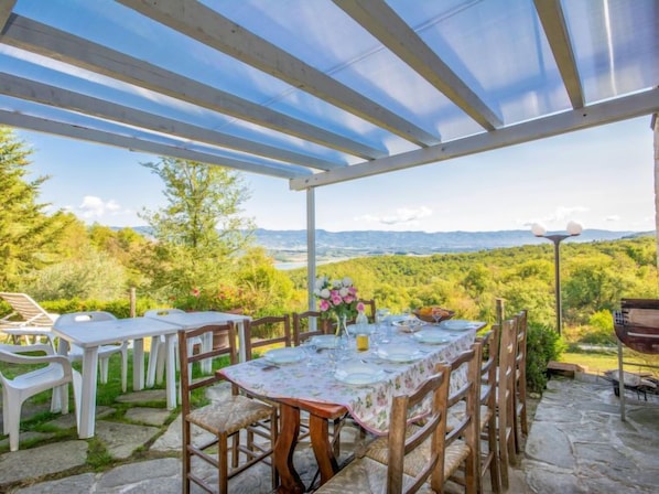 Une terrasse extérieure avec une table dressée pour le repas, entourée d’un sol en pierre et de chaises en bois, donnant sur un paysage luxuriant.