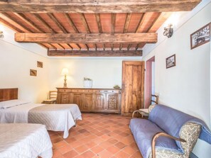 Una habitación con dos camas, un armario de madera, un sofá y suelo de baldosas.