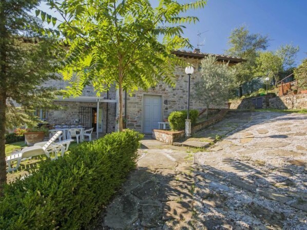 Un edificio de piedra con una puerta, un pequeño jardín con un banco y un patio empedrado.