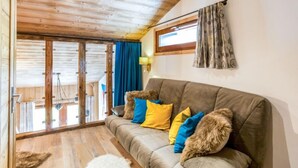 A cozy living room with a wooden ceiling, a grey sofa with colorful cushions, a fluffy rug, and a sliding glass door leading to an outdoor area. - Grand Roc (Val Claret) by Interhome (Tignes)