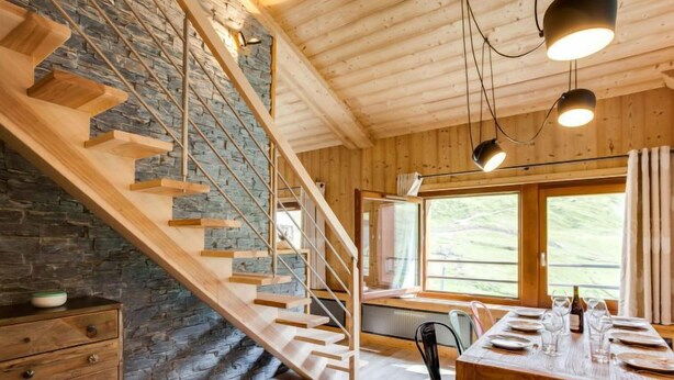 A wooden staircase with a stone wall, a dining area with a table set for four, and a window with a view of the outdoors. - Grand Roc (Val Claret) by Interhome (Tignes)