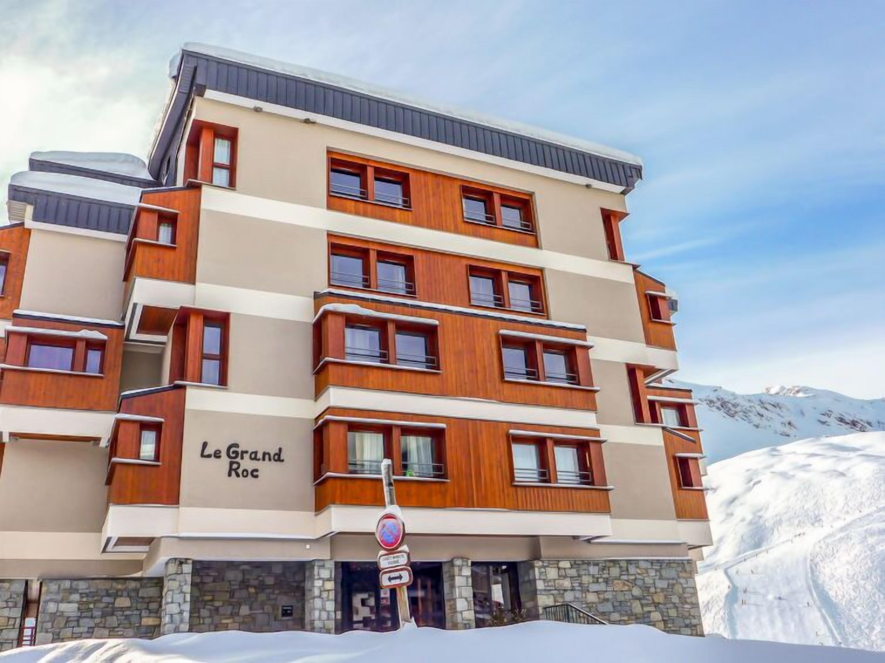A multi-story hotel with a wooden facade and a stone base, named "Le Grand Roc".