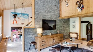 A spacious living area with a stone wall, wooden furniture, a fireplace, and a mounted television. - Grand Roc (Val Claret) by Interhome (Tignes)