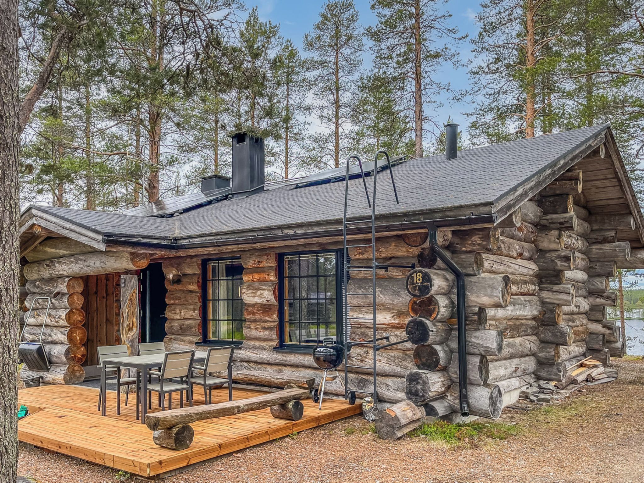Eine Blockhütte mit einer Terrasse, Sitzgelegenheiten im Freien und Blick auf einen See.