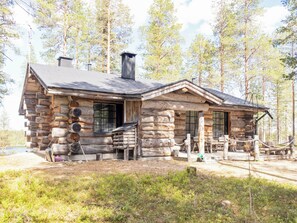 Une cabane en rondins avec une cheminée, une véranda et une vue sur la forêt environnante.