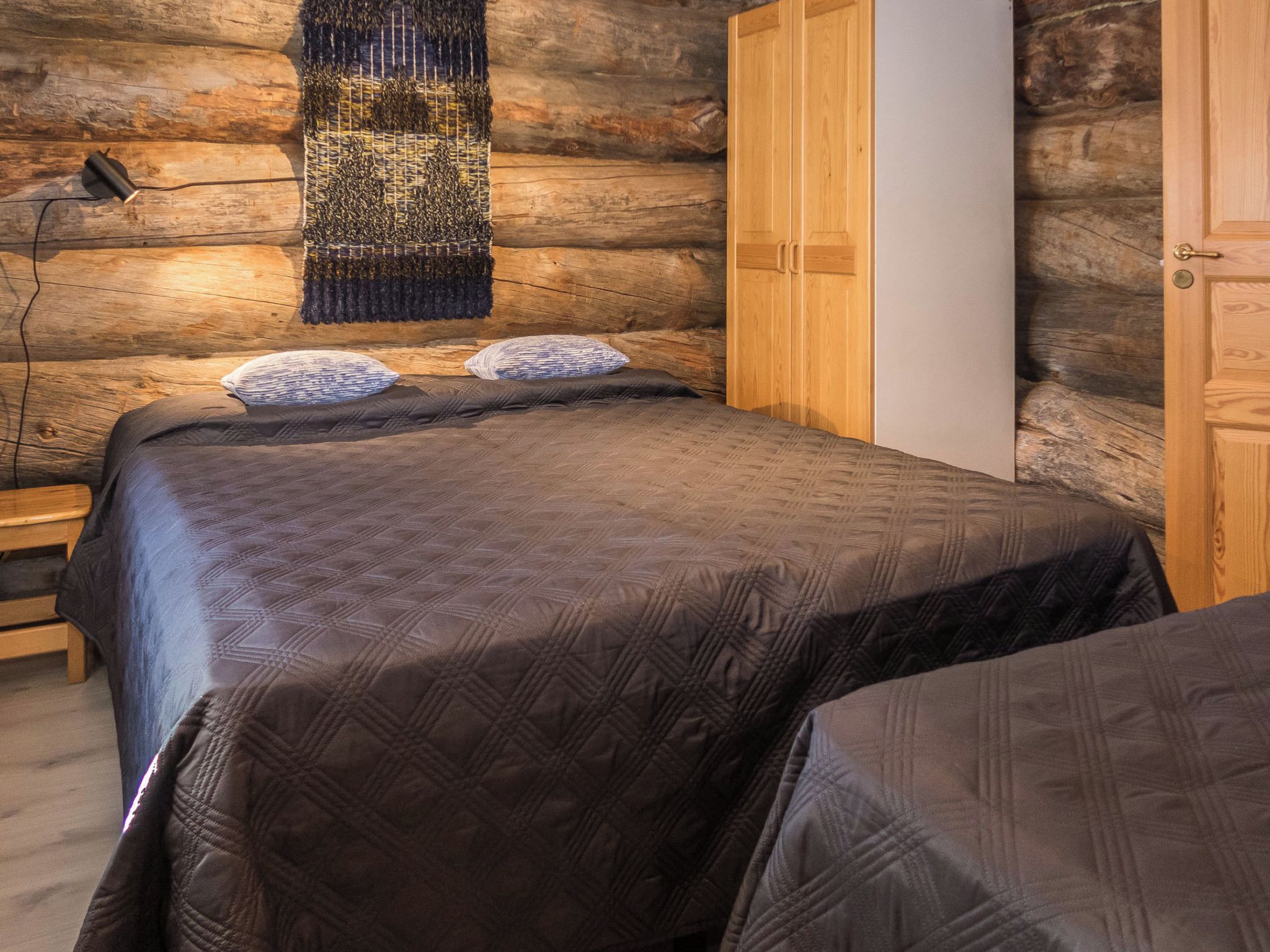 Une chambre dans une cabane en rondins, avec un lit, un banc et une armoire.