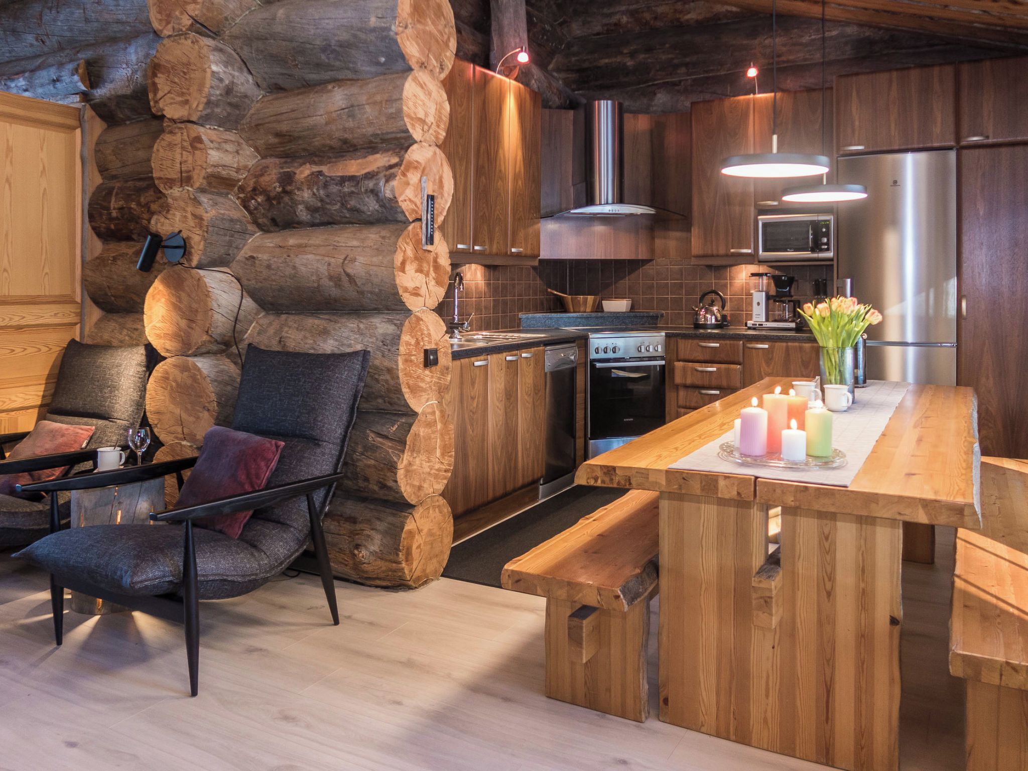 Une cuisine rustique avec des troncs d’arbres servant de revêtement mural, une table à manger décorée de bougies et un fourneau moderne.