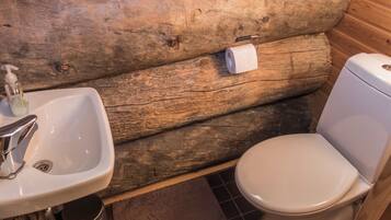 Une salle de bain rustique avec un mur en rondins de bois, un lavabo blanc et des toilettes.