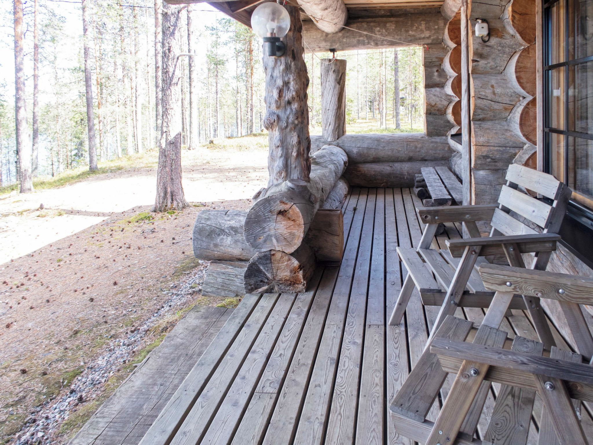 Une terrasse en bois, agrémentée de bancs et de troncs d’arbres, entourée d’une forêt.