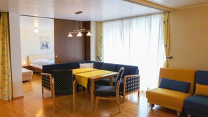 A room with a wooden floor, a sofa, a dining table with chairs, a bed, and a window with curtains. - Appartmenthaus Skyline 309 by Interhome (St. Moritz)