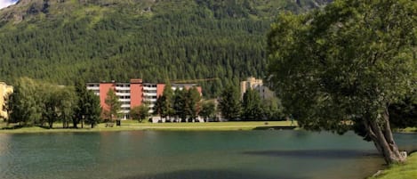 Ein Hotel mit roter Fassade, am See gelegen, mit Bergen im Hintergrund.