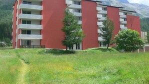 A multi-story building with balconies, surrounded by a grassy area and trees, with mountains in the background. - Appartmenthaus Skyline 309 by Interhome (St. Moritz)