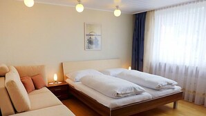 A bedroom with a bed, a nightstand, a lamp, a sofa, and a window with curtains. - Appartmenthaus Skyline 309 by Interhome (St. Moritz)