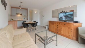 Een moderne woonkamer met een bank, een salontafel, een televisie en een eethoek met stoelen en een tafel.