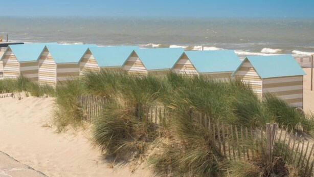 Een rij strandhutten met gestreepte daken en een zandstrand op de voorgrond.