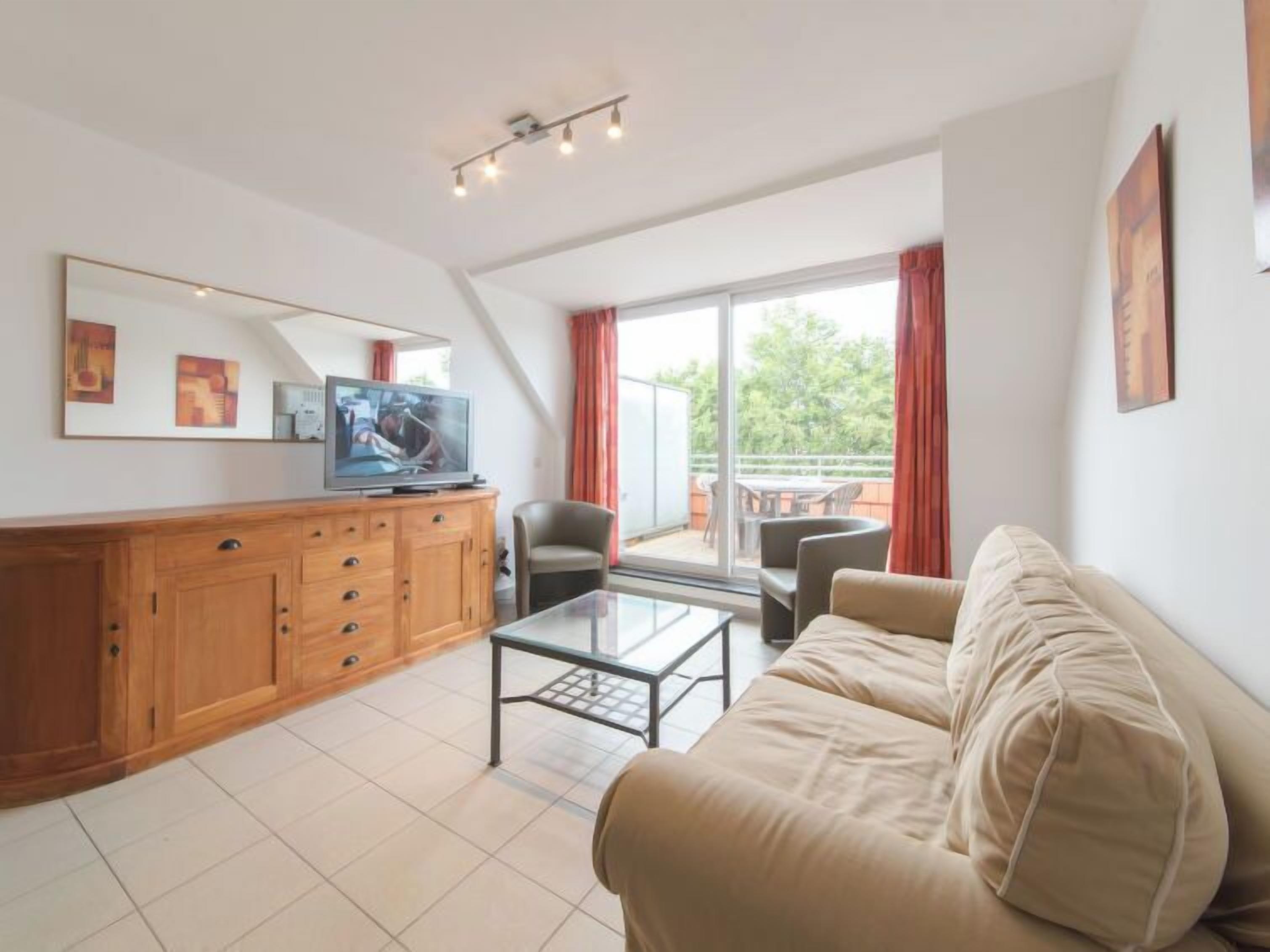 A modern living room with a sofa, a coffee table, a TV on a wooden cabinet, and a balcony with red curtains.