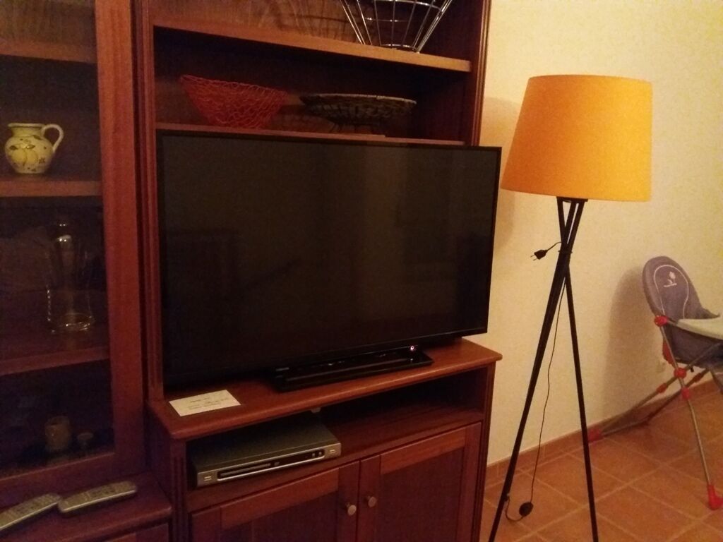 A television on a wooden stand with a shelf above it containing decorative items.