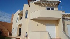 A modern two-story building with a flat roof, a balcony on the upper floor, and a garage door on the ground floor. - Wonderful villa composed of 3 bedrooms with wardrobes, 2 complete bathrooms. (Foz do Arelho)