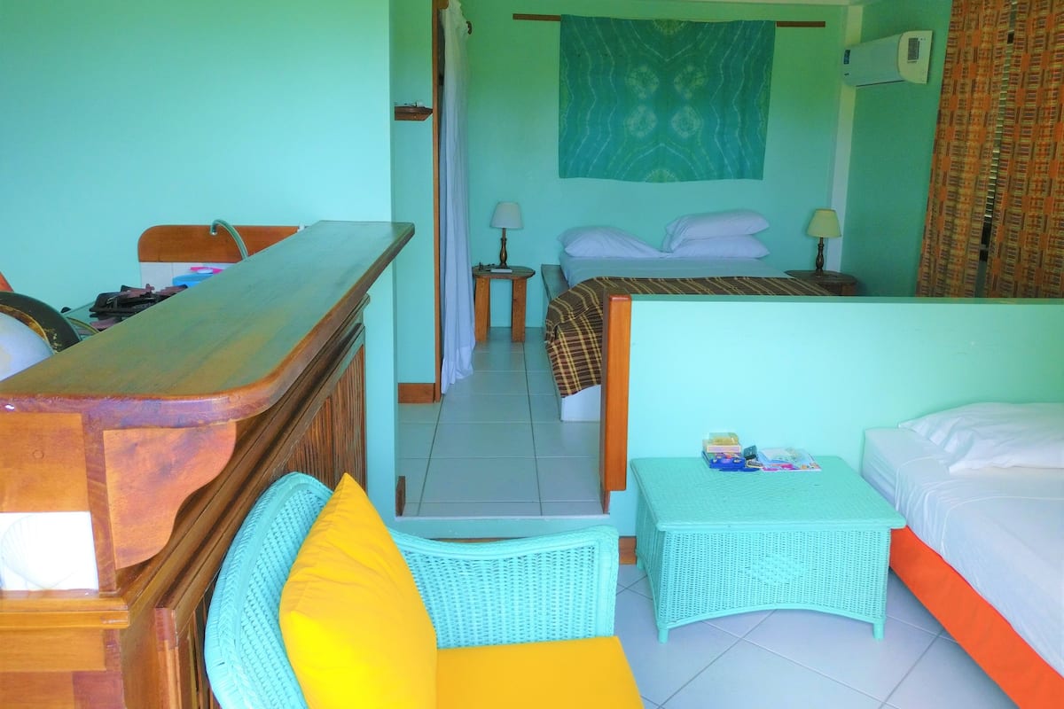 Une chambre d’hôtel avec un bureau en bois, un lit avec une literie blanche, une petite table avec une lampe et une chaise en osier.