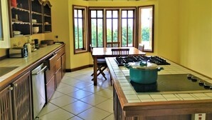 A kitchen with a central island, a dining table, and large windows. - Tobago Hibiscus Villas and Apartments (Bethel)