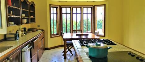 A kitchen with a central island, a dining table, and large windows.
