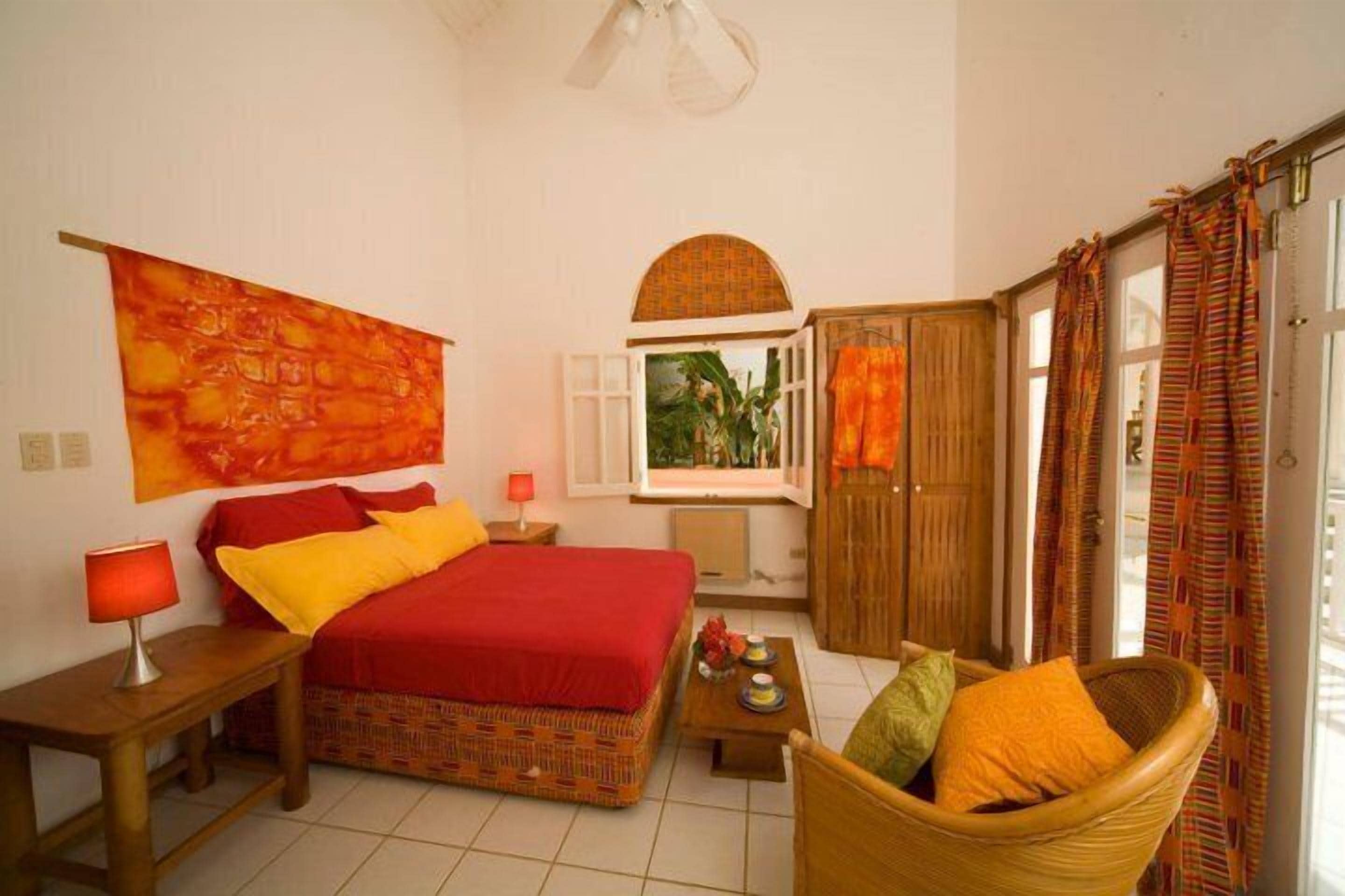 A bedroom with a bed, a chair, a nightstand, a window with curtains, and a wall with a tapestry.