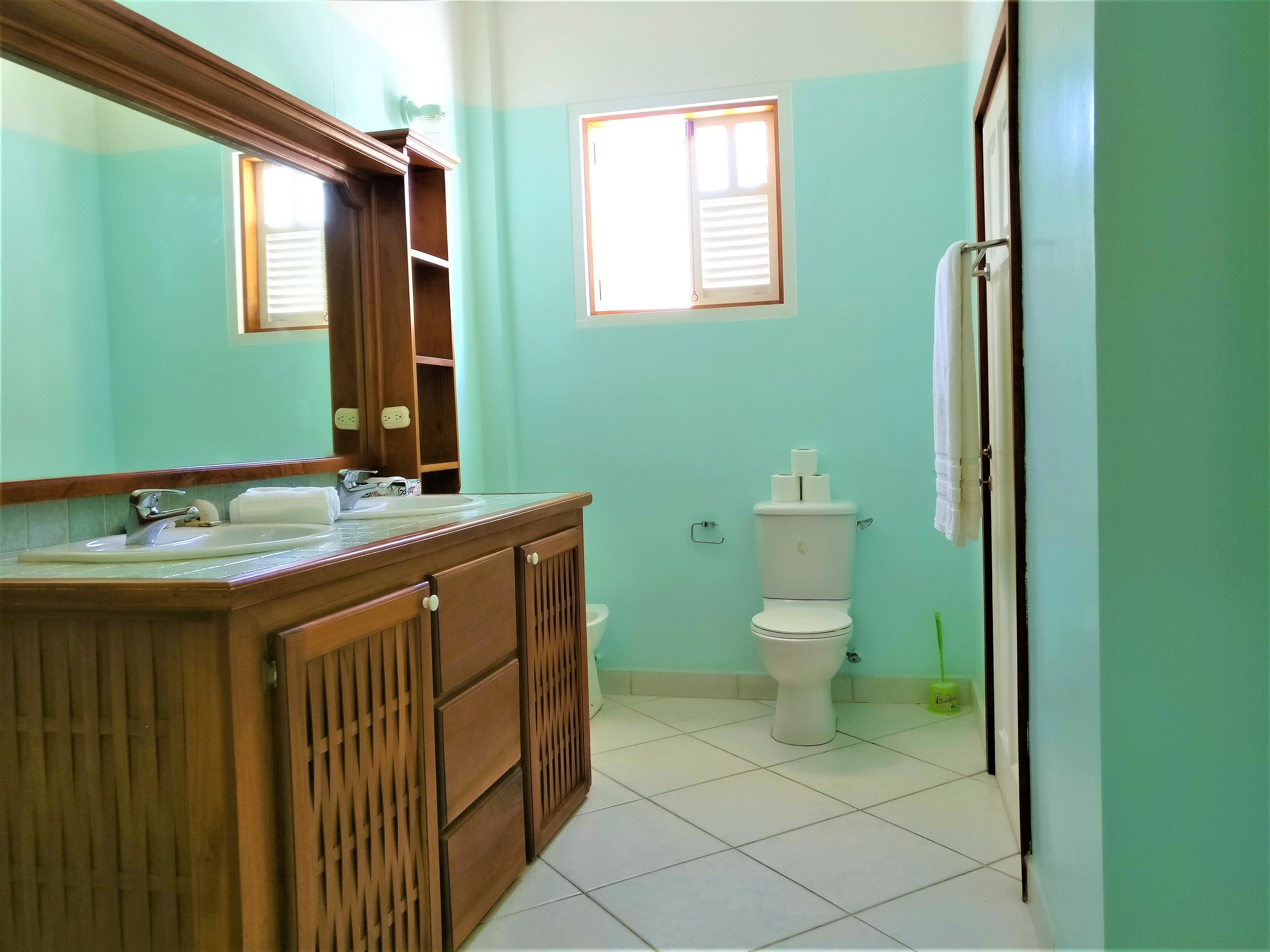 A bathroom with a wooden vanity, a sink, a mirror, a toilet, and a window.
