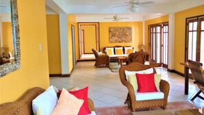 A spacious living area with a high ceiling, wicker furniture, and a large painting on the wall. - Tobago Hibiscus Villas and Apartments (Bethel)