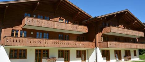 A multi-story wooden chalet with balconies, large windows, and a well-maintained lawn.