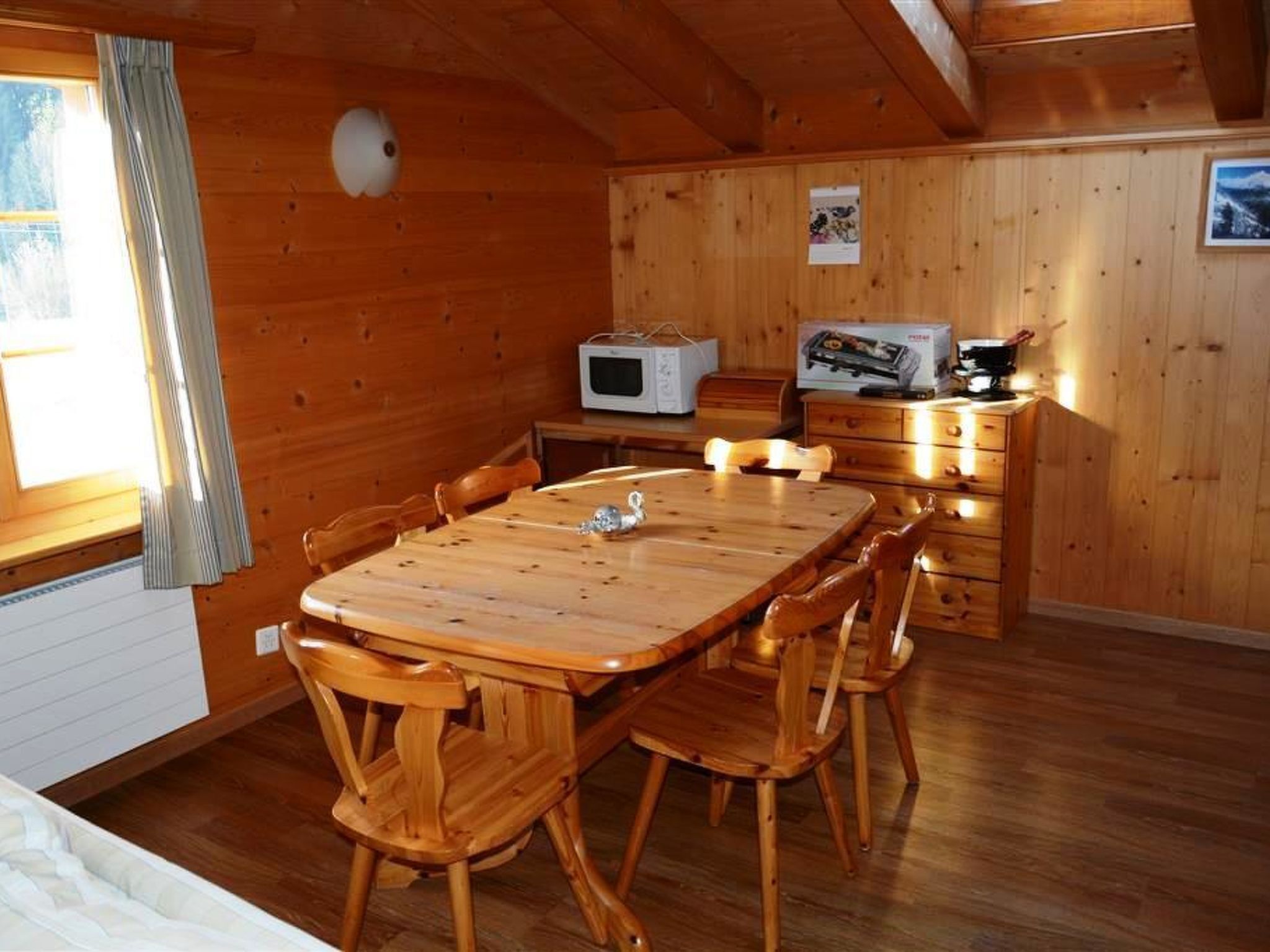 A wooden cabin interior with a dining table and chairs, a microwave, and a television.