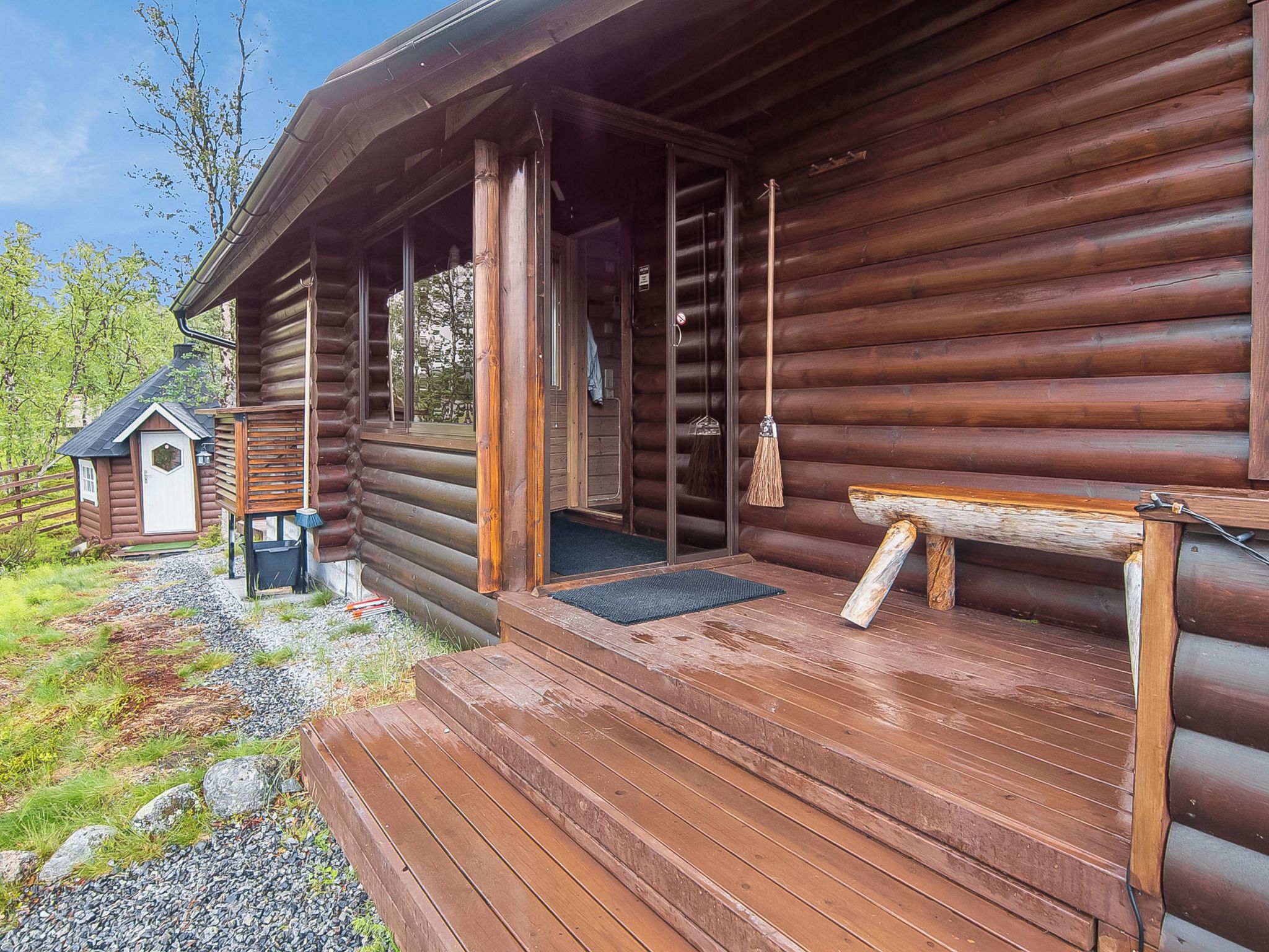 Une cabane en rondins avec un porche en bois, une petite dépendance attenante et un chemin de gravier menant à l’entrée.