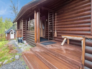 Une cabane en rondins avec un porche en bois, une petite dépendance attenante et un chemin de gravier menant à l’entrée.
