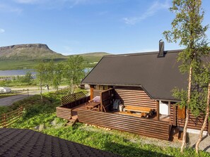 Una cabaña de troncos con terraza, chimenea y vistas a un lago y montañas.