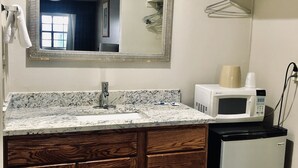 Une salle de bain avec un lavabo en marbre, un meuble-lavabo en bois, un miroir, un four à micro-ondes et un petit réfrigérateur.