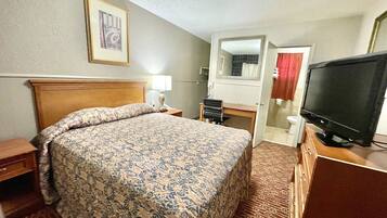 Une chambre d’hôtel avec un grand lit, un bureau, une télévision et une salle de bain visible à travers une porte ouverte.