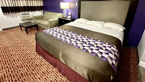 Une chambre d’hôtel avec un grand lit, une moquette à motifs, un canapé, un bureau et une fenêtre avec des rideaux.