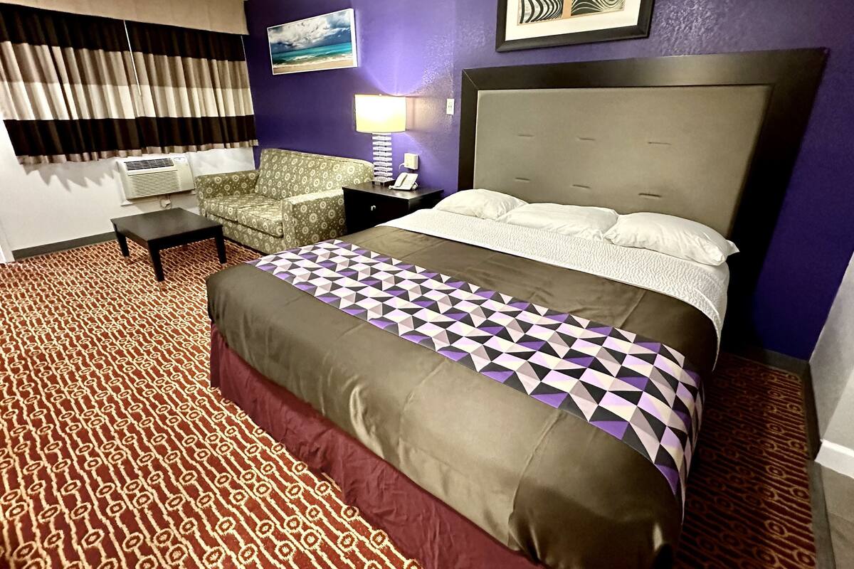 Ett hotellrum med en stor säng, en mönstrad matta, en soffa, ett skrivbord och ett fönster med gardiner.