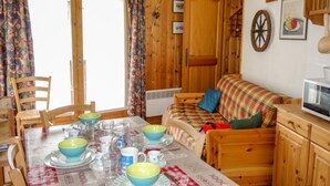 A cozy cabin-style room with a wooden interior, a dining table set with bowls and glasses, a sofa with a plaid blanket, and a vintage radio.