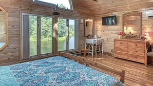 A cabin with a large bed, a wooden dresser, a vanity, and a table with a chair.