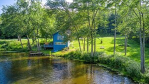 A blue house by a calm river surrounded by lush greenery.