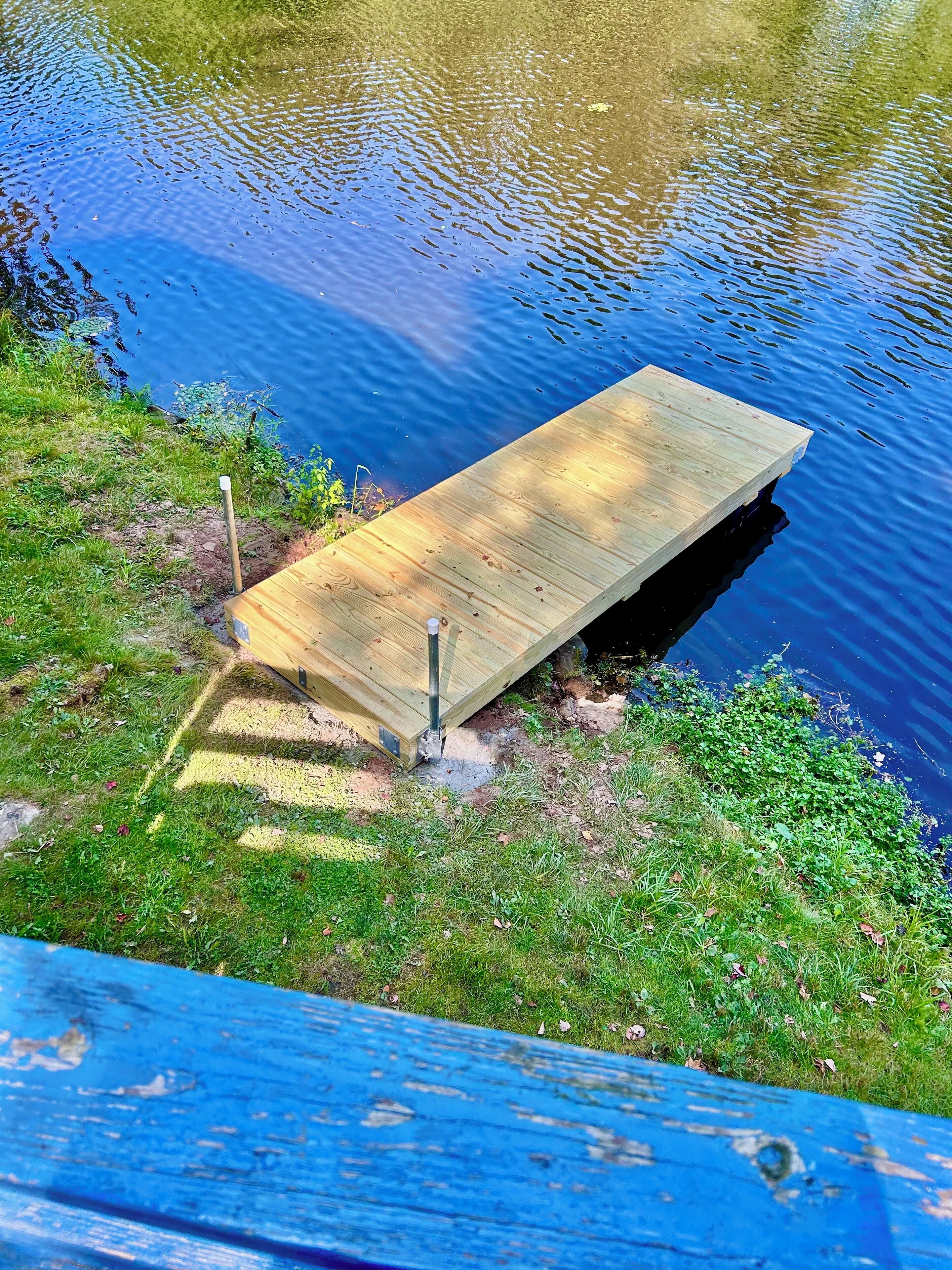 Una banchina di legno si estende in uno specchio d'acqua, circondata da zone erbose.