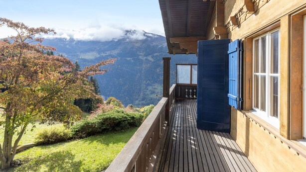 Un balcon en bois offrant une vue sur les montagnes et les couleurs automnales des arbres.