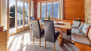 Une cabane en bois comprenant un coin repas, un banc et de grandes fenêtres donnant sur les montagnes.
